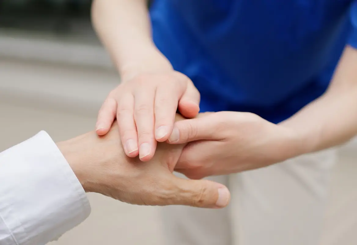 高齢女性の手を介護職員が両手で包んでいる写真